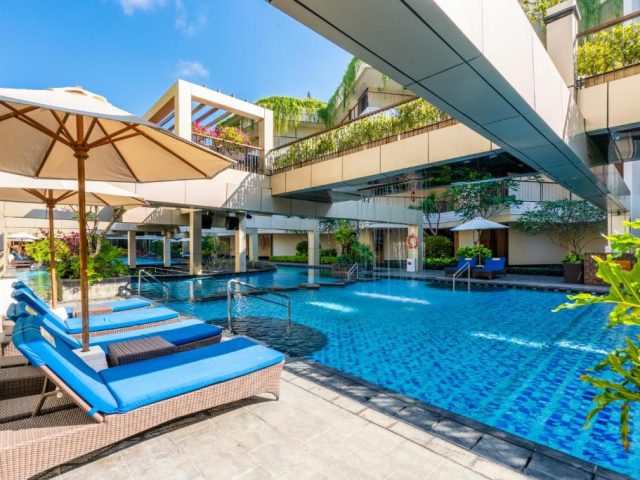 Pool area with loungers, an umbrella, and palms at Vouk Hotel & Suites